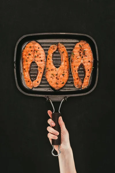 Tiro cortado de pessoa segurando grelha com bifes de salmão gourmet em preto — Fotografia de Stock