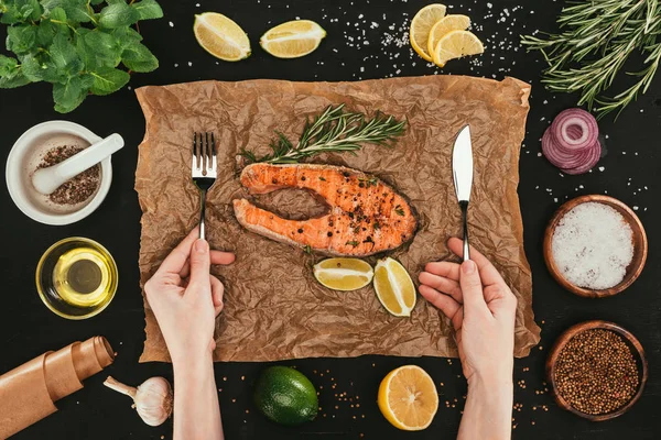 Tiro cortado de persona con tenedor y cuchillo comer filetes de salmón - foto de stock