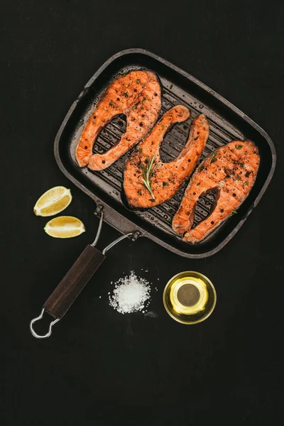 Top view of salmon steaks on grill, salt, olive oil and lime slices on black — Stock Photo