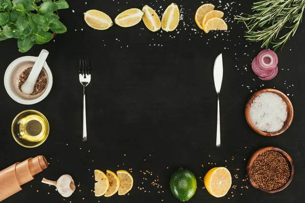 Top view of cutlery and various spices and seasonings on black with copy space — Stock Photo