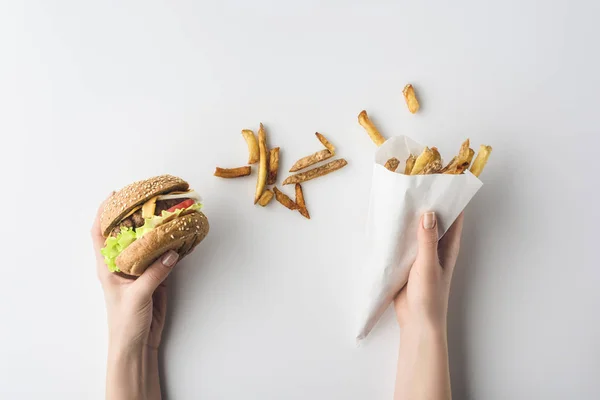 Обрізаний вид рук з гамбургером і картоплею фрі в паперовому конусі, ізольовані на білому — стокове фото