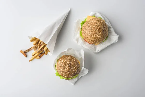 Vista superior de papas fritas en cono de papel y dos hamburguesas, aisladas en blanco - foto de stock