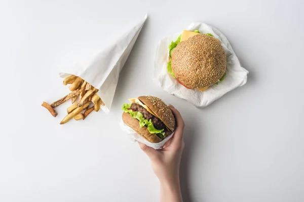 Ausgeschnittene Ansicht weiblicher Hand mit Hamburgern und Pommes in Papiertüte, isoliert auf weiß — Stockfoto