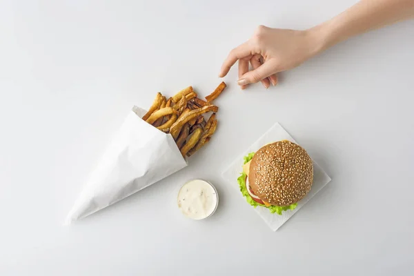 Cropped view of female hand with french fries, homemade hamburger and mayonnaise, isolated on white — Stock Photo