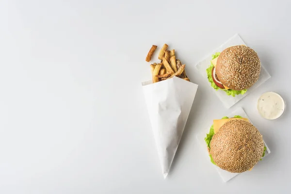 Vista dall'alto di patatine fritte in cono di carta, due hamburger e maionese, isolate su bianco — Foto stock