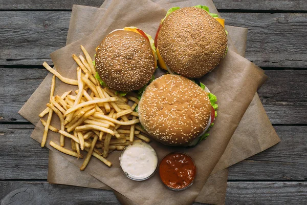Vista superior de hamburguesas, papas fritas, ketchup y mayonesa sobre papel de hornear sobre mesa de madera — Stock Photo