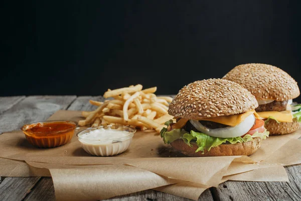 Cheeseburgers maison traditionnels sur papier cuisson avec frites, ketchup et sauces mayonnaise — Photo de stock