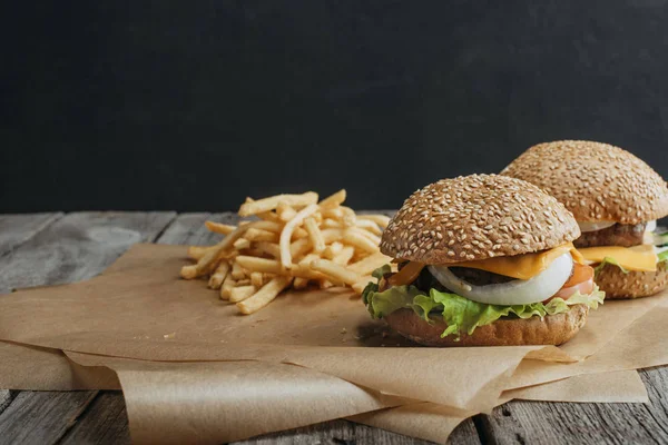 Traditional homemade cheeseburgers on baking paper with french fries — Stock Photo