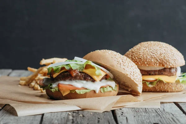 Tasty homemade cheeseburgers on baking paper with french fries — Stock Photo