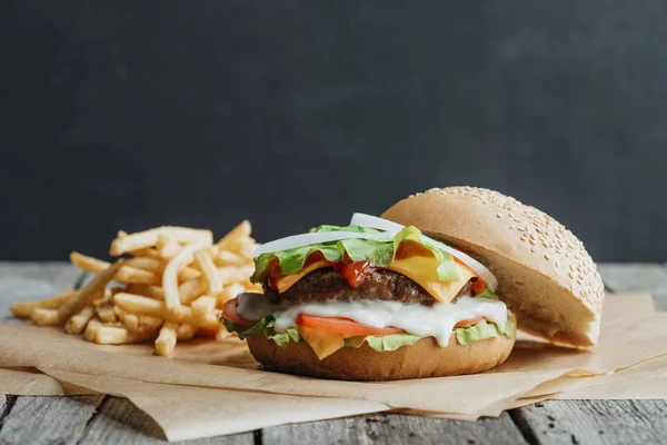 Hamburguesa casera tradicional sobre papel de hornear con papas fritas — Stock Photo