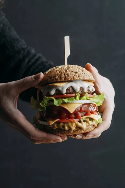 Vista recortada de manos femeninas con hamburguesa casera grande de queso — Stock Photo