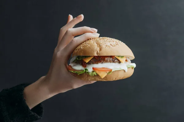 Vista recortada de la mano con hamburguesa casera gourmet con queso en negro - foto de stock