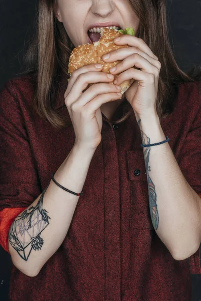 Vista ritagliata di ragazza tatuata mordere gustoso hamburger — Foto stock