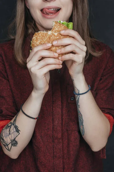 Cropped view of tattooed girl eating tasty hamburger — Stock Photo