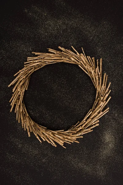Top view of golden wreath made of sticks on black surface — Stock Photo