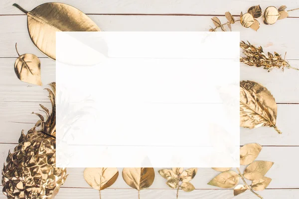 Vue de dessus de coloré en doré diverses feuilles et ananas avec du papier blanc au milieu sur table en bois — Photo de stock