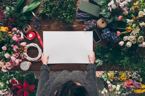 Imagen recortada de floristería sosteniendo hoja de papel vacía en las manos sobre la mesa de trabajo - foto de stock