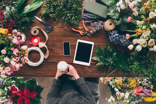 Immagine ritagliata del fiorista che tiene il caffè nella tazza di carta sopra il posto di lavoro — Foto stock