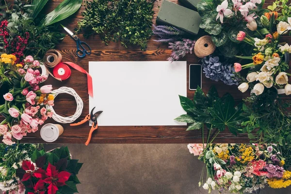Top view of empty sheet of paper on wooden table among flowers — Stock Photo