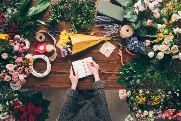 Image recadrée de fleuriste écrire quelque chose au carnet de travail — Photo de stock