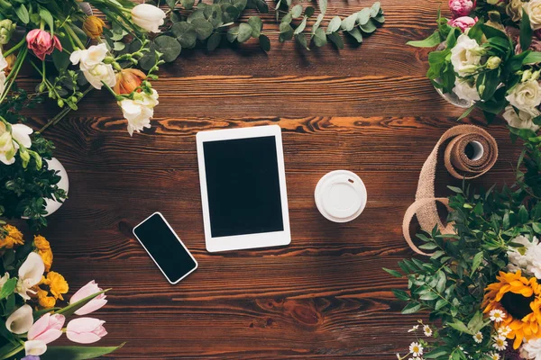 Vista superior de dispositivos digitales y café en taza de papel en la mesa de floristería de madera - foto de stock