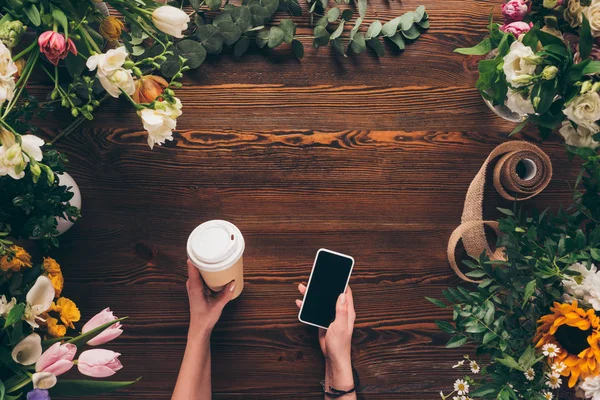 Immagine ritagliata di fiorista che tiene il caffè in tazza di carta e smartphone in mano — Foto stock