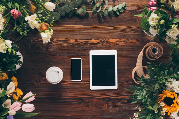 Top view of coffee in paper cup, smartphone and tablet on table with flowers — Stock Photo