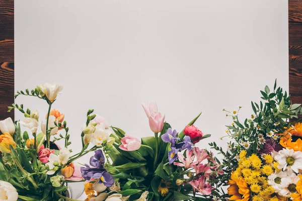 Vista superior de la hoja de papel vacía blanca con flores de colores en la mesa de madera - foto de stock