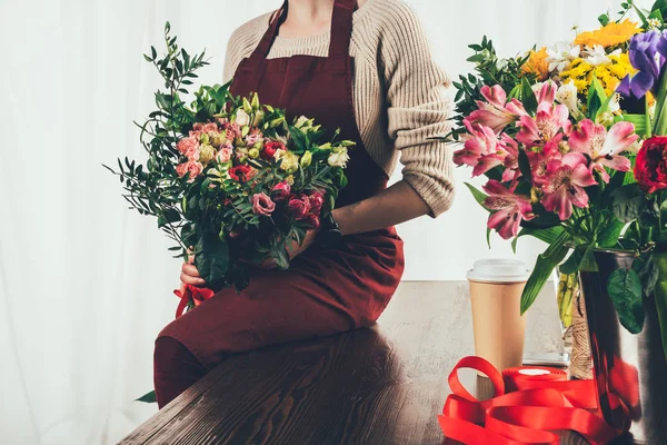 Cropped image of florist sitting on table and holding bouquet in hands — Stock Photo