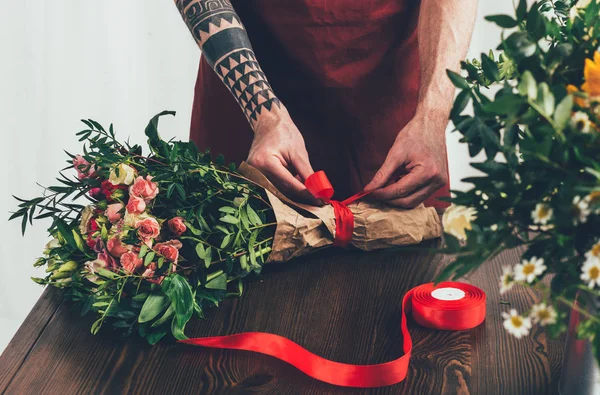 Cropped image of male tattooed florist tying ribbon on bouquet — Stock Photo
