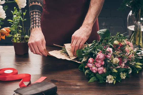 Imagem recortada de florista masculino com tatuagem no buquê de embrulho mão em papel de embalagem — Fotografia de Stock