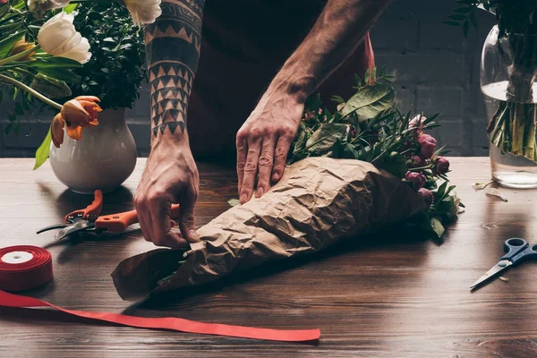 Cropped image of male florist wrapping bouquet in pack paper — Stock Photo