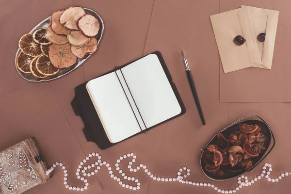 Vista superior del cuaderno, joyero, frutas secas y sobres sobre fondo de papel marrón - foto de stock