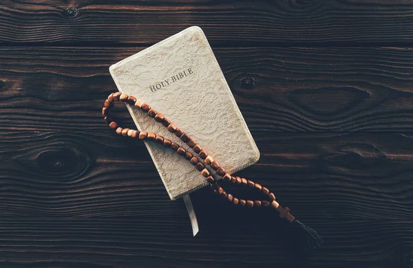 Верхний вид закрытой священной библии и четки с крестом на деревянном столе — стоковое фото