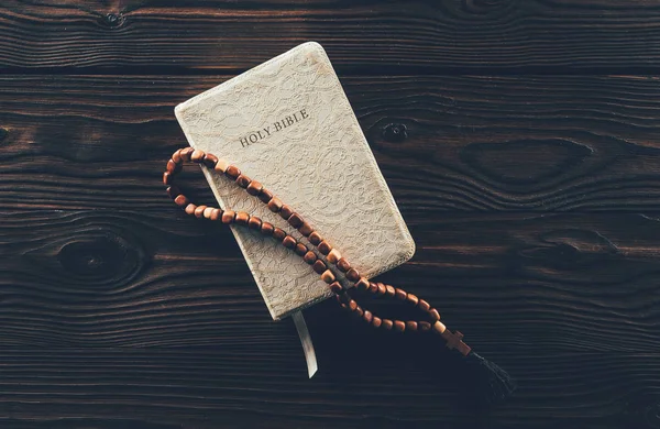 Vista superior de la biblia santa cerrada y del rosario con la cruz en la mesa de madera - foto de stock