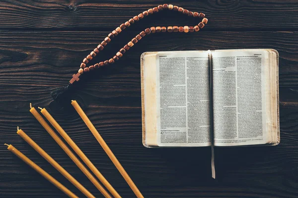 Vue de dessus de la bible sainte ouverte avec chapelet et bougies sur la table — Photo de stock