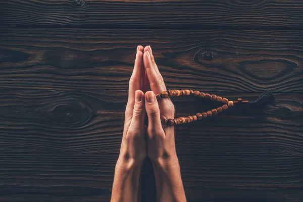 Cropped image of woman holding rosary and praying at table — Stock Photo