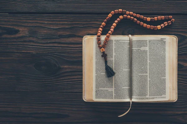 Vue de dessus de la bible sainte ouverte avec chapelet sur table en bois — Photo de stock