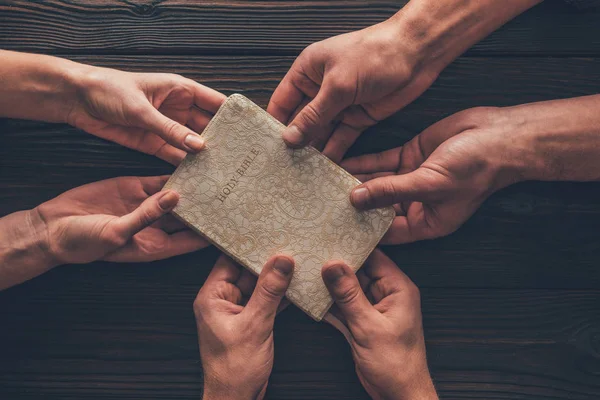 Cropped image of woman and men holding one bible — Stock Photo