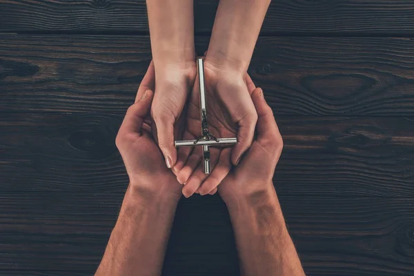 Cropped image of woman and man holding christian cross in hands — Stock Photo