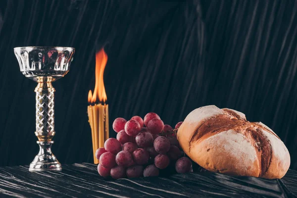 Хлеб с виноградом, чаша и свечи на черной ткани, Святое причастие — стоковое фото