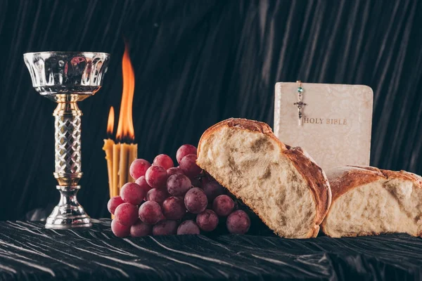 Хліб, Біблія, чаші і християнський хрест на чорний столик, Святе причастя — стокове фото