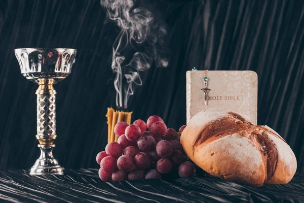 Еда, библия, чаша и христианский крест на темном столе для Святого Причастия — стоковое фото