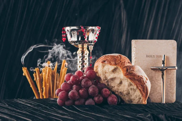 Heilige Bibel und christliches Kreuz mit Kerzen und Kelch auf dunkel gestreiftem Tisch zur Kommunion — Stockfoto