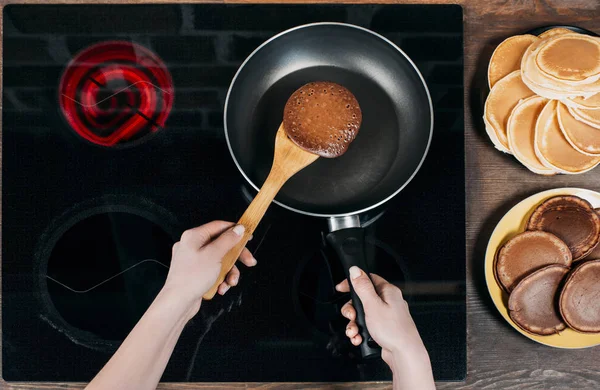 Cropped shot of woman flipping pancake on frying pan with wooden spatula — Stock Photo