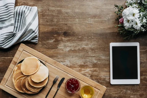 Верхний вид завтрака с блинами и цифровой планшет на деревянный стол — стоковое фото