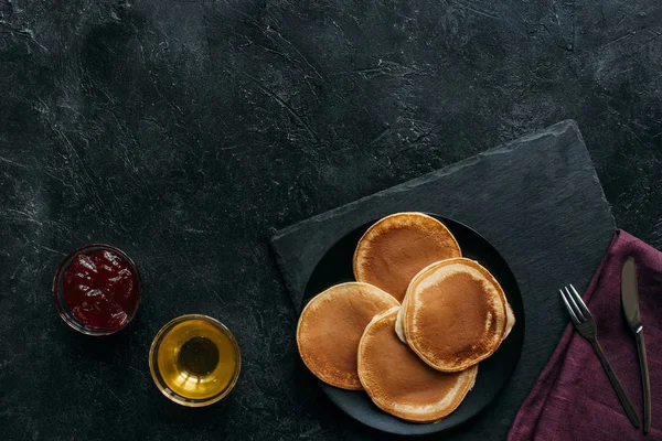 Top view of pancakes with jam and maple syrup on black concrete surface — Stock Photo