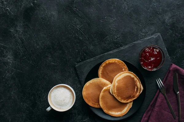 Top view of freshly baked pancakes with jam and coffee on black surface — Stock Photo