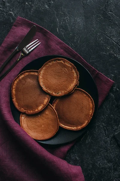 Vista superior del plato de panqueques de chocolate con cubiertos en servilleta roja - foto de stock