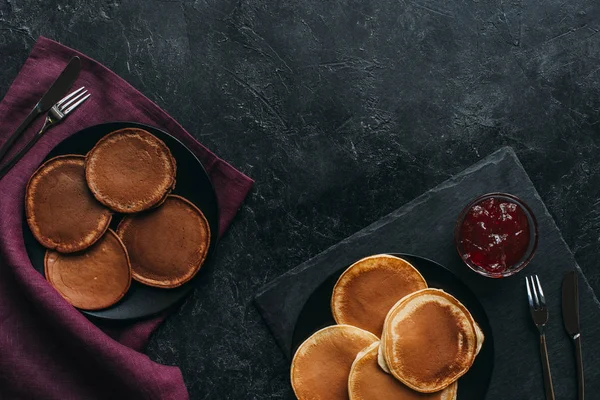 Top view of various pancakes in plates on black surface — Stock Photo